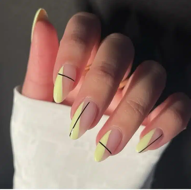 Unhas decoradas com esmalte amarelo claro e linhas pretas geométricas