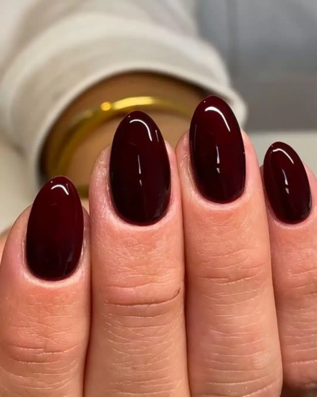 Unhas com esmalte vinho escuro em formato oval, mostrando acabamento brilhante.