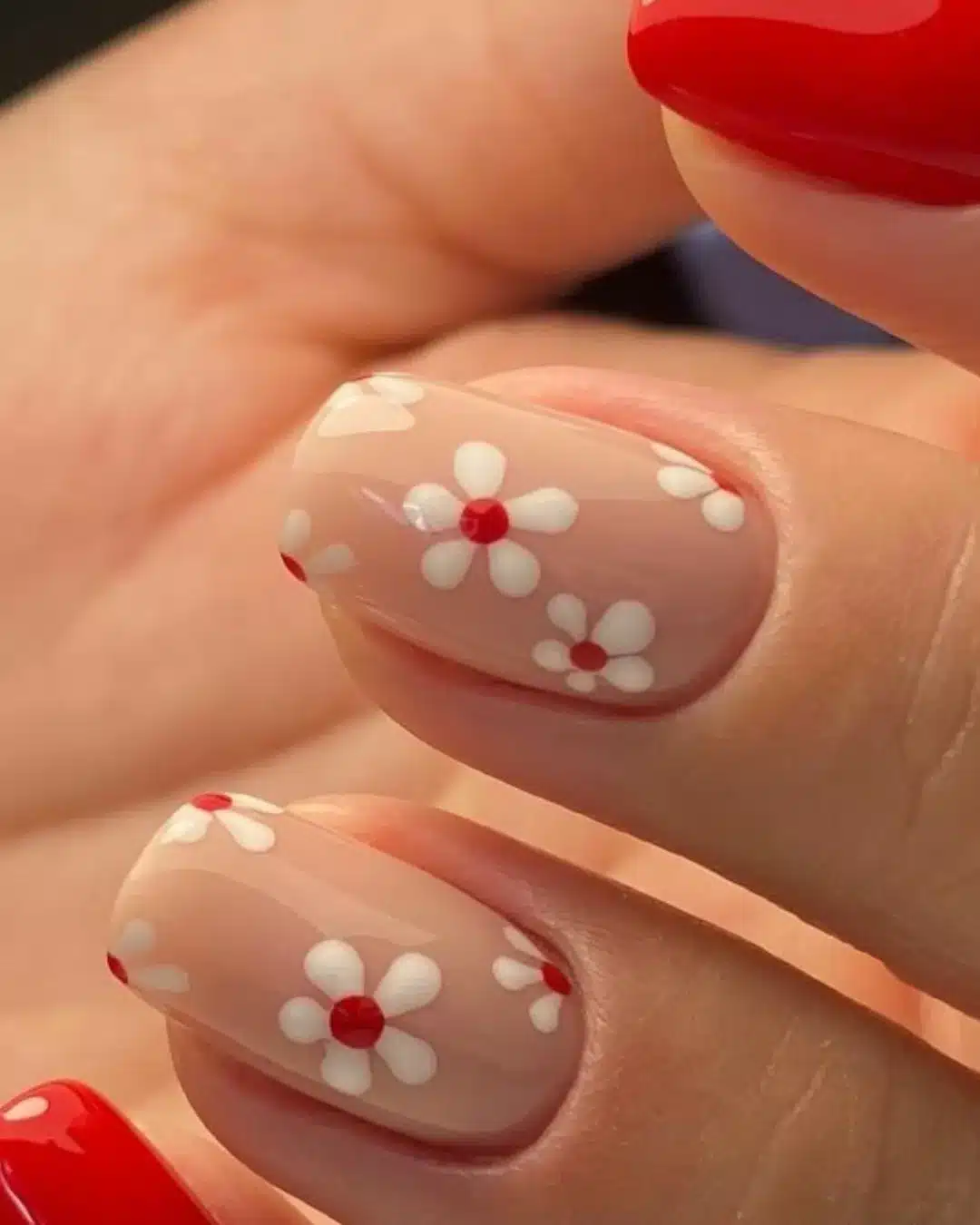 Unhas decoradas com flores vermelhas e brancas em fundo nude.