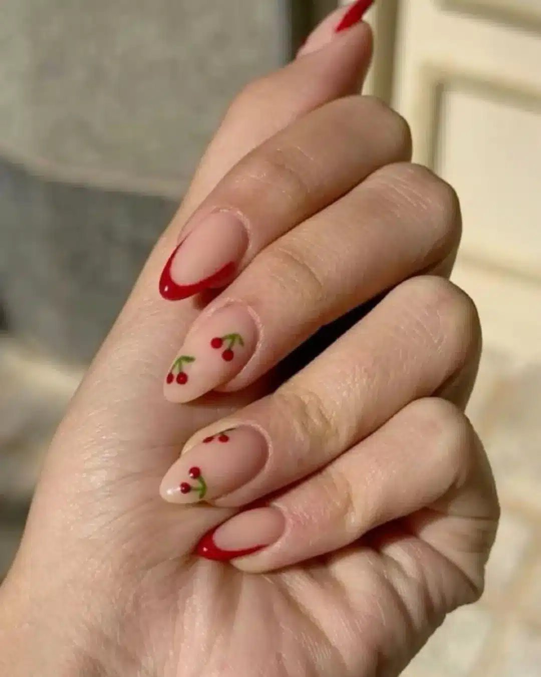 Unhas com francesinha vermelha e detalhes de cerejas vermelhas delicadas.