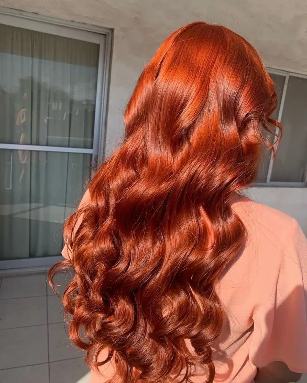 Cabelo longo com ondas em tom vermelho acobreado com técnica balayage, iluminado pelo sol.