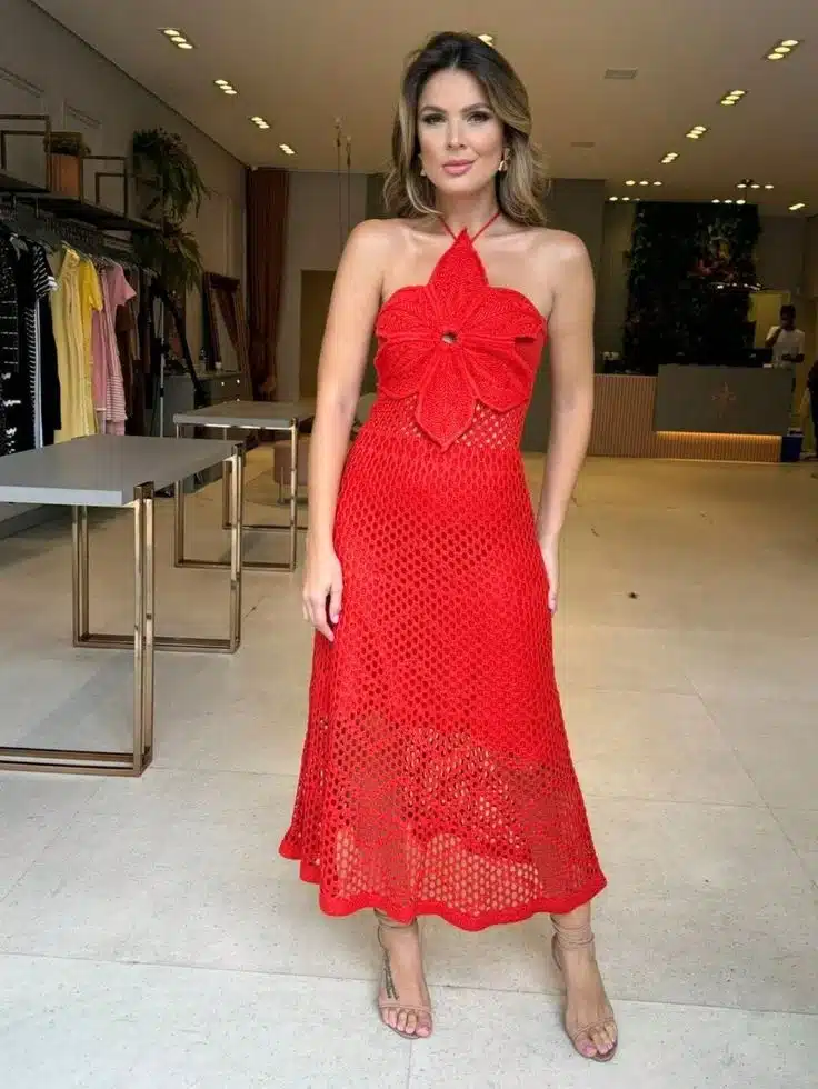 Mulher usando vestido de crochê vermelho vibrante com detalhes florais no busto.