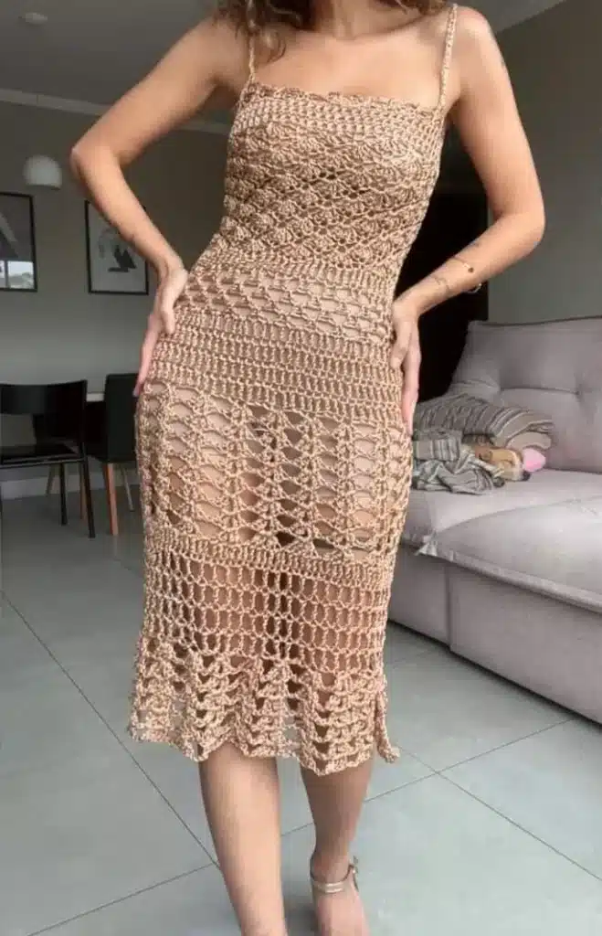 Mulher usando vestido midi de crochê bege com padrão vazado e alças finas.