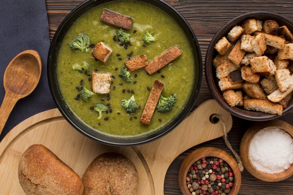 Sopa de caldo verde com croutons e brócolis, acompanhada de pães.