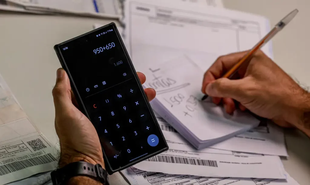 Pessoa calculando contas com celular e caderno durante organização financeira