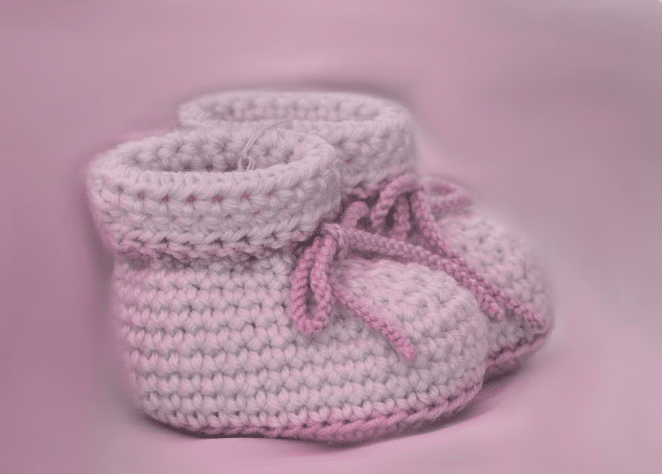 Sapatinhos de bebê em crochê rosa com cadarço, sobre fundo rosa