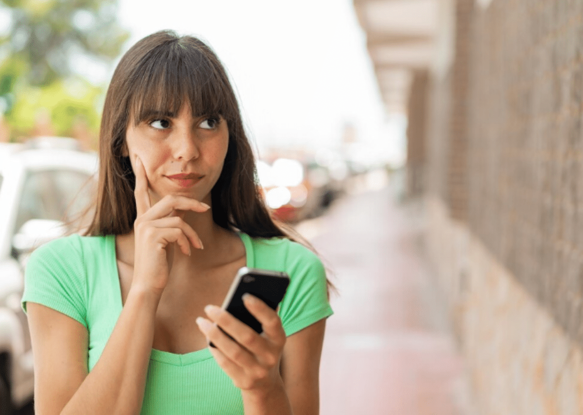 Mulher segurando celular com expressão de dúvida em ambiente urbano