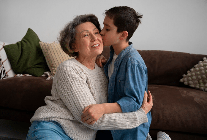 Neto dando um beijo carinhoso na avó enquanto se abraçam no chão da sala.