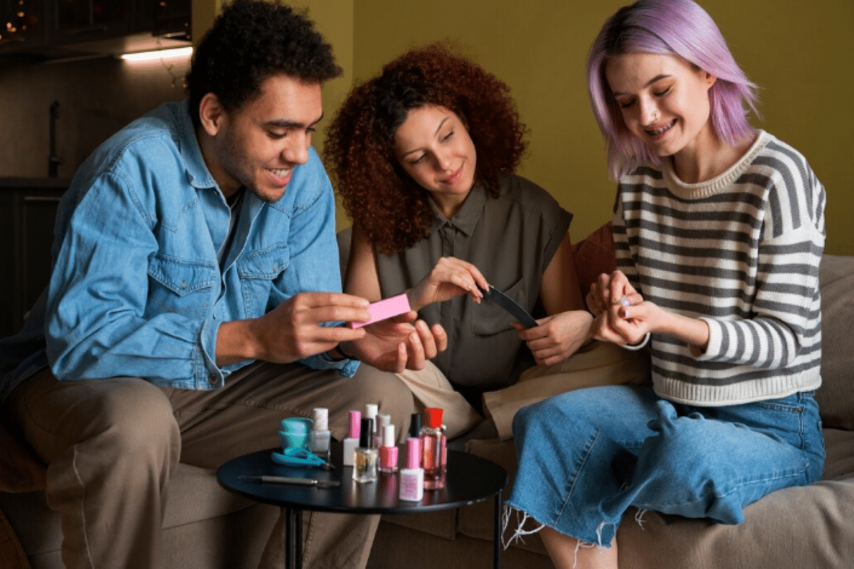 Três pessoas se divertem fazendo as unhas juntas com esmaltes e acessórios sobre a mesa.