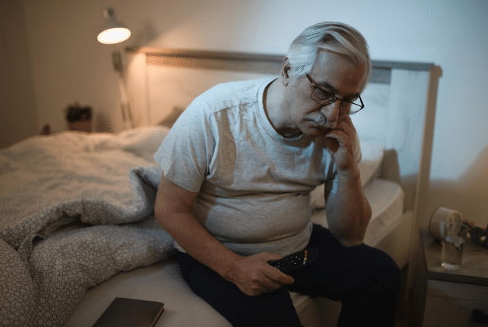 Idoso sentado na cama com expressão de cansaço e insônia