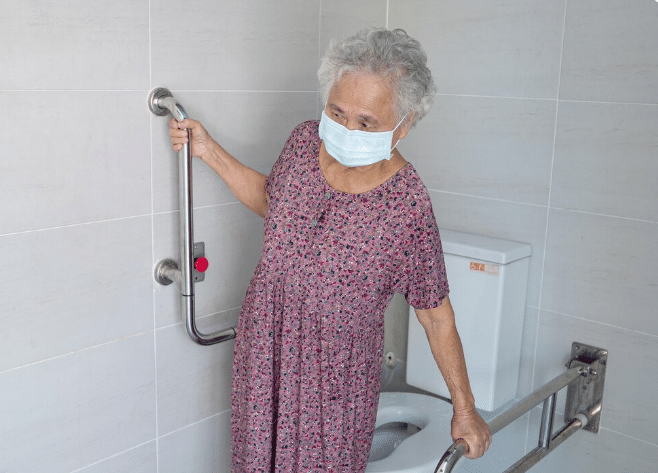 Idosa usando barra de apoio no banheiro com máscara de proteção