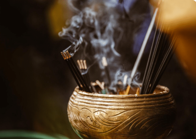 Incensos acesos pandoc soltando fumaça em suporte artesanal dourado