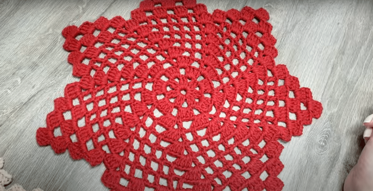 Centro de mesa em crochê vermelho com ponto aberto sobre superfície de madeira