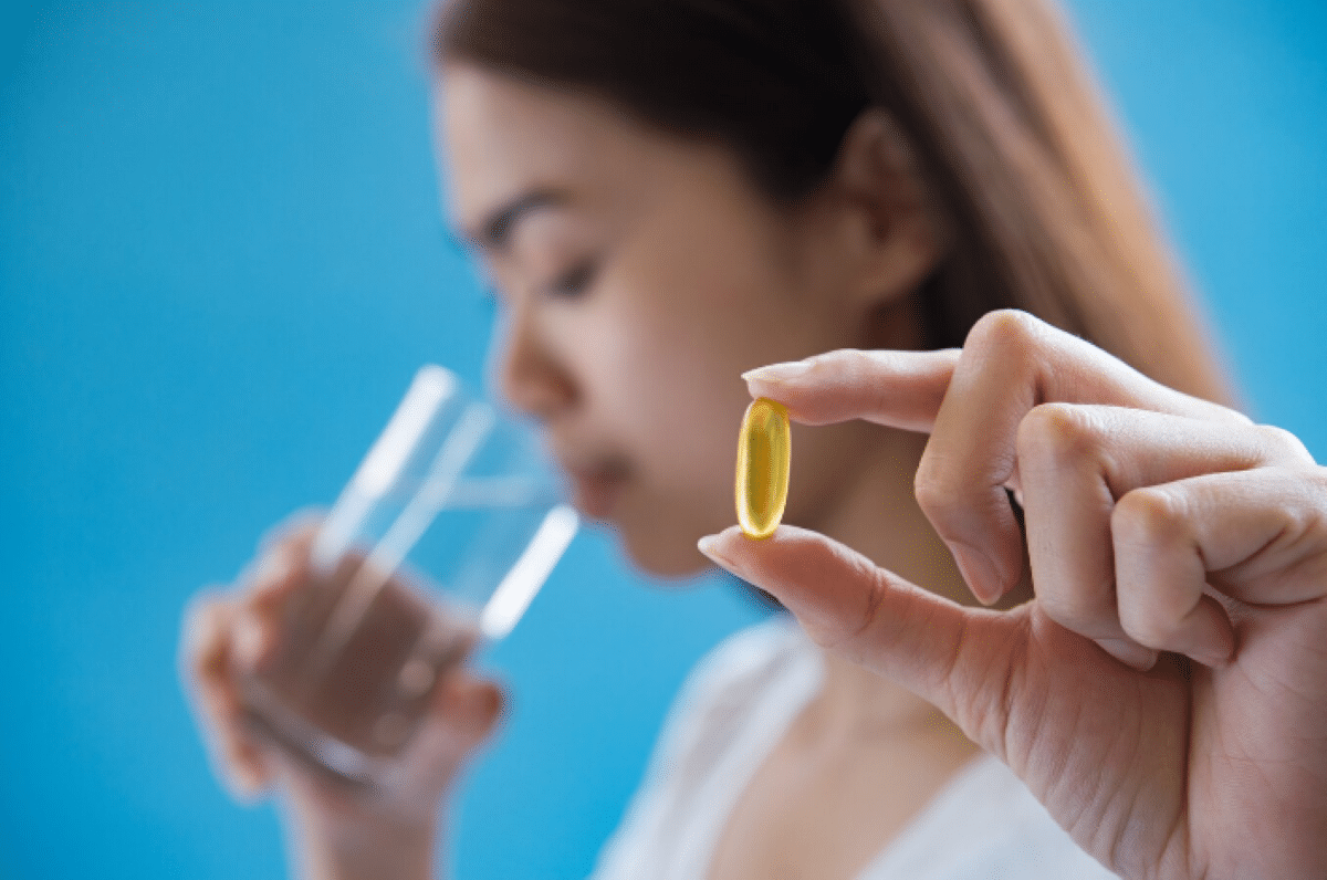 Mulher segurando cápsula de suplemento e copo com água para ingestão