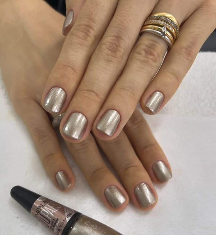 Unhas curtas esmaltadas com tom metálico prateado e acabamento elegante