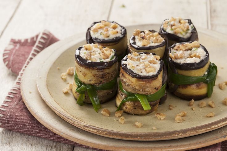 Rolinhos de berinjela recheados com ricota e nozes servidos em prato rústico