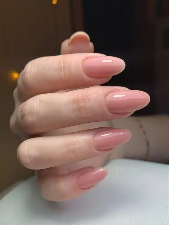 Unhas com esmalte nude rosado, acabamento translúcido e formato arredondado, refletindo um estilo delicado e discreto.
