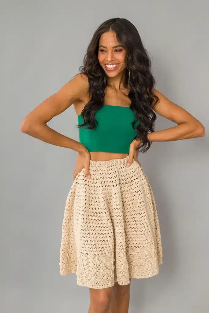 Saia godê de crochê bege com top verde, em pose descontraída, destacando o design de crochê da saia.