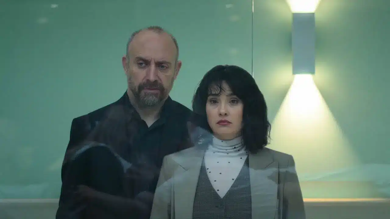 Cena de suspense da série turca 'Amantes Anônimos', mostrando dois personagens em uma sala de observação.