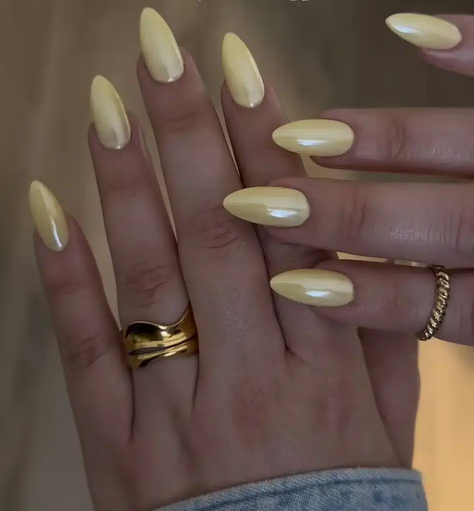 Unhas com esmalte amarelo manteiga perolado em acabamento delicado