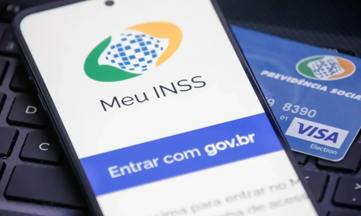 Aplicativo Meu INSS aberto no celular ao lado de cartão da Previdência Social