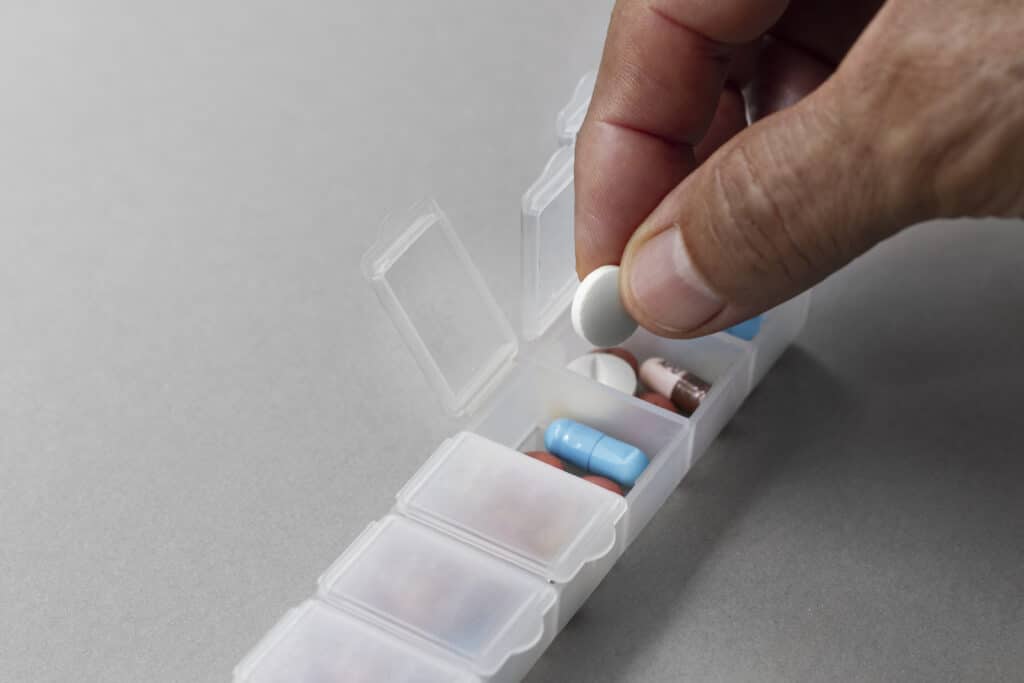 Mão organizando comprimidos em caixa de medicação semanal