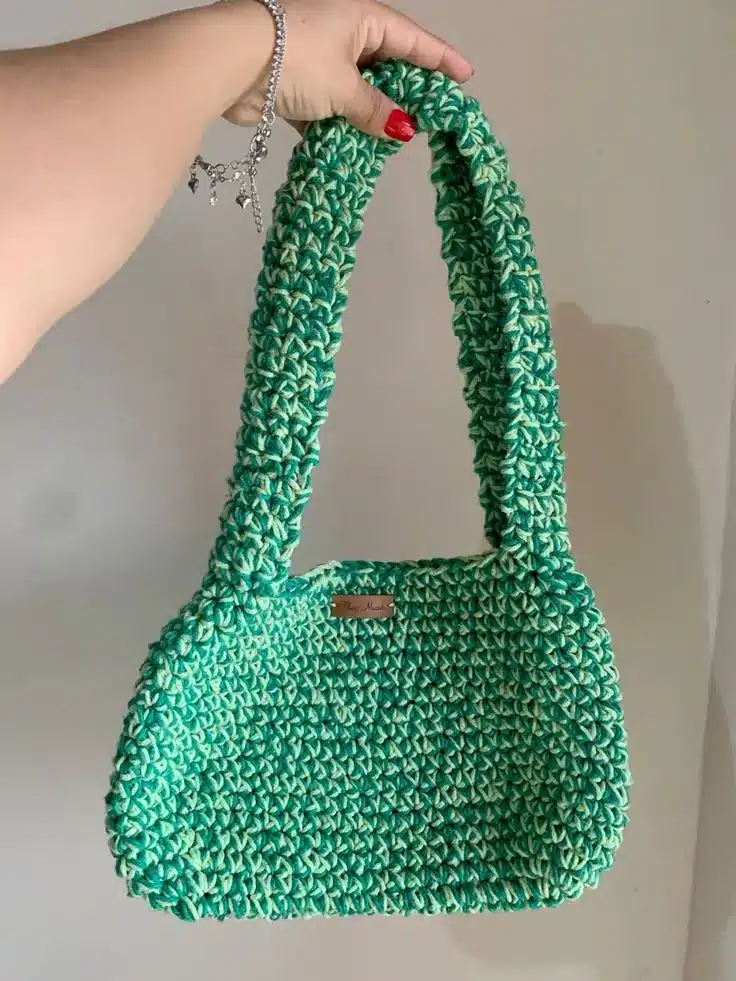 Bolsa simples de crochê em verde e creme, com alça larga e formato retangular.