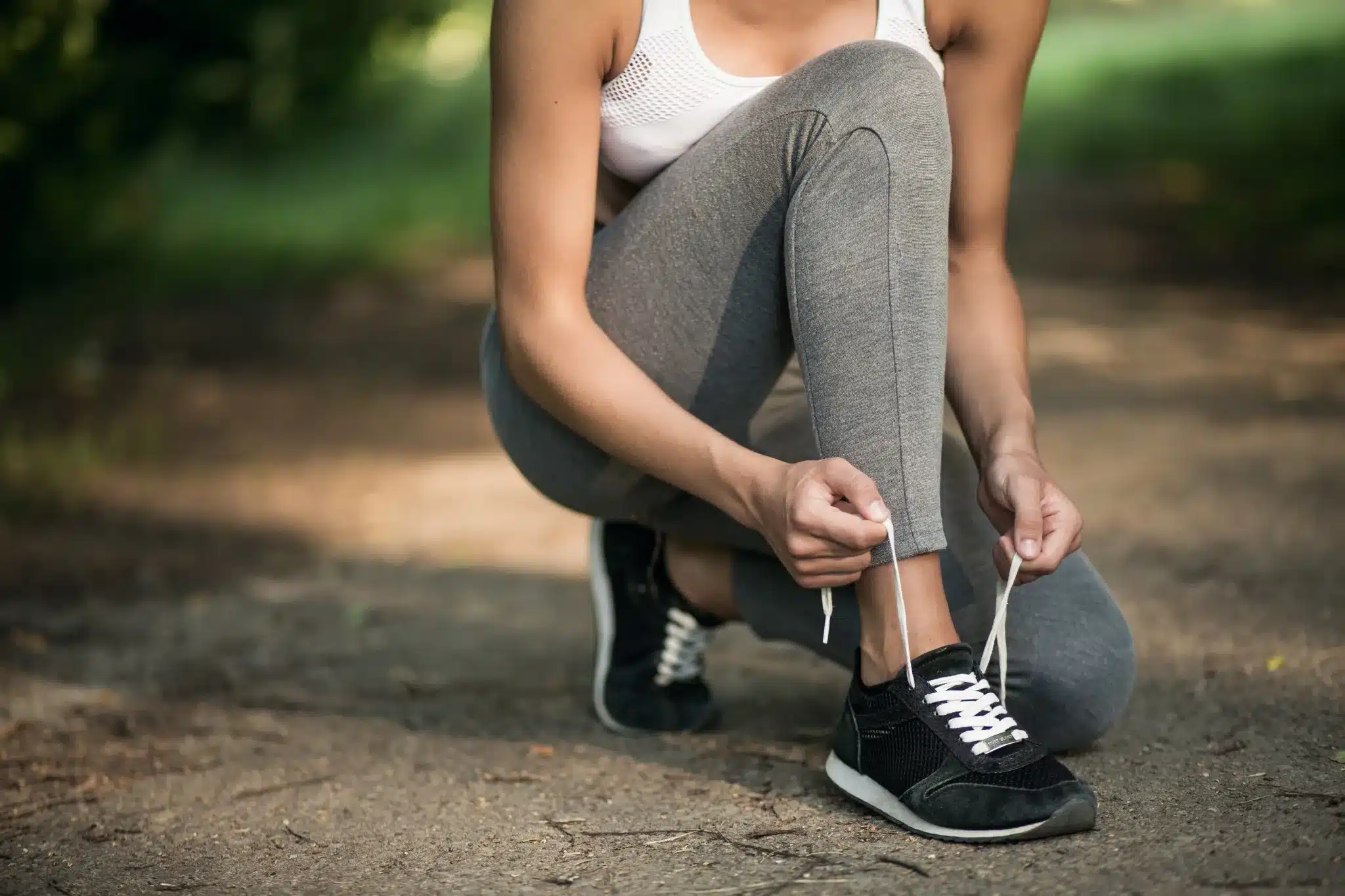 Mulher ajustando o cadarço do tênis em ambiente ao ar livre, buscando conforto no calçado.
