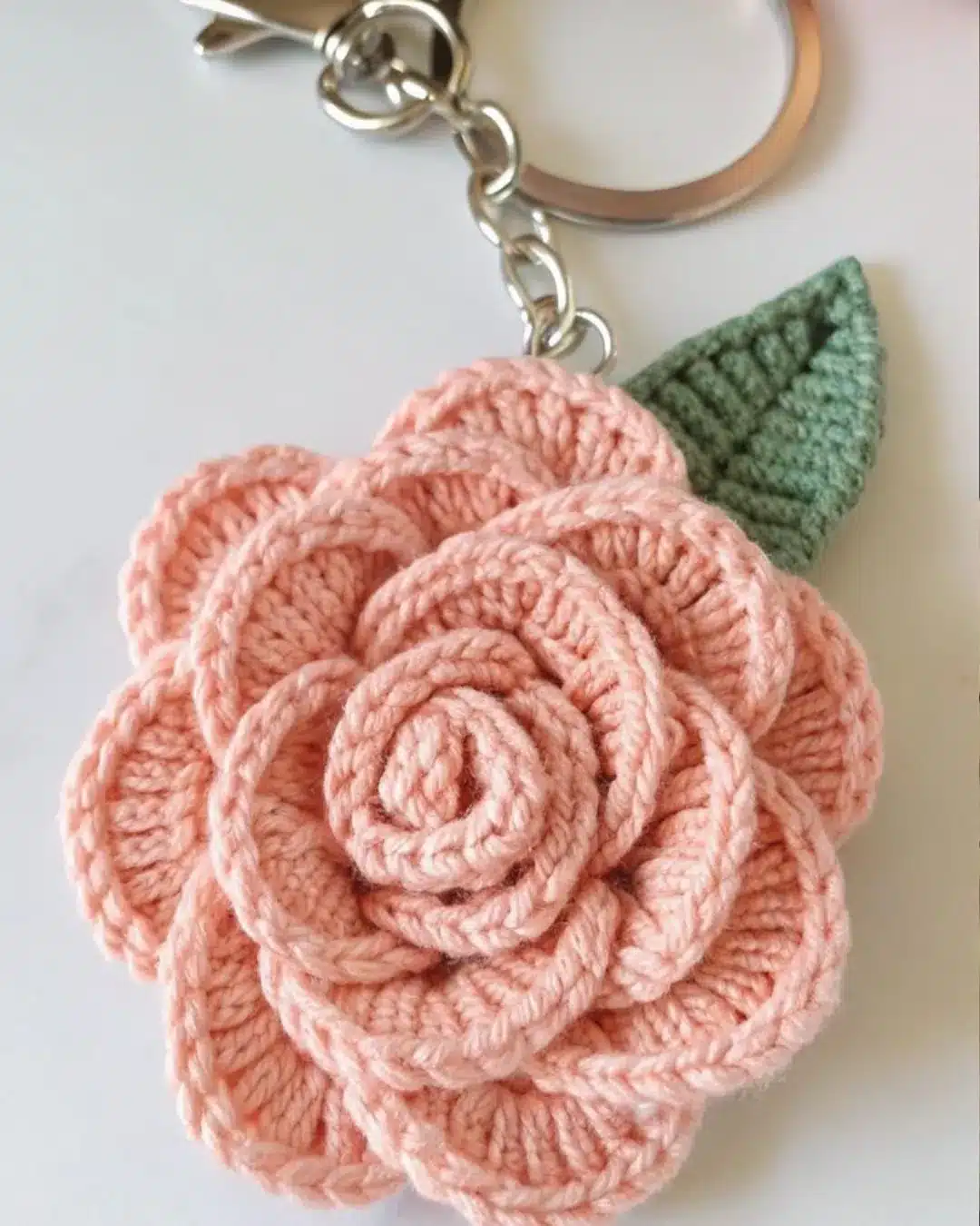 Chaveiro artesanal de crochê em formato de flor rosa com folha verde.