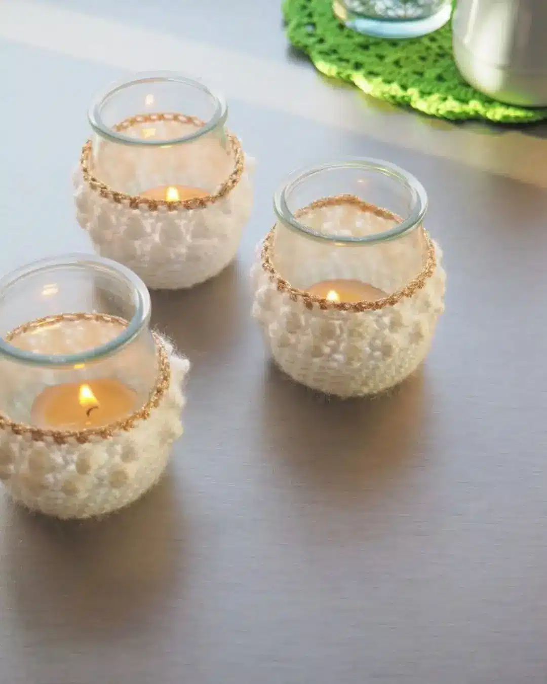 Luminárias feitas com vidro e crochê, com velas acesas no centro, em um ambiente tranquilo e acolhedor.