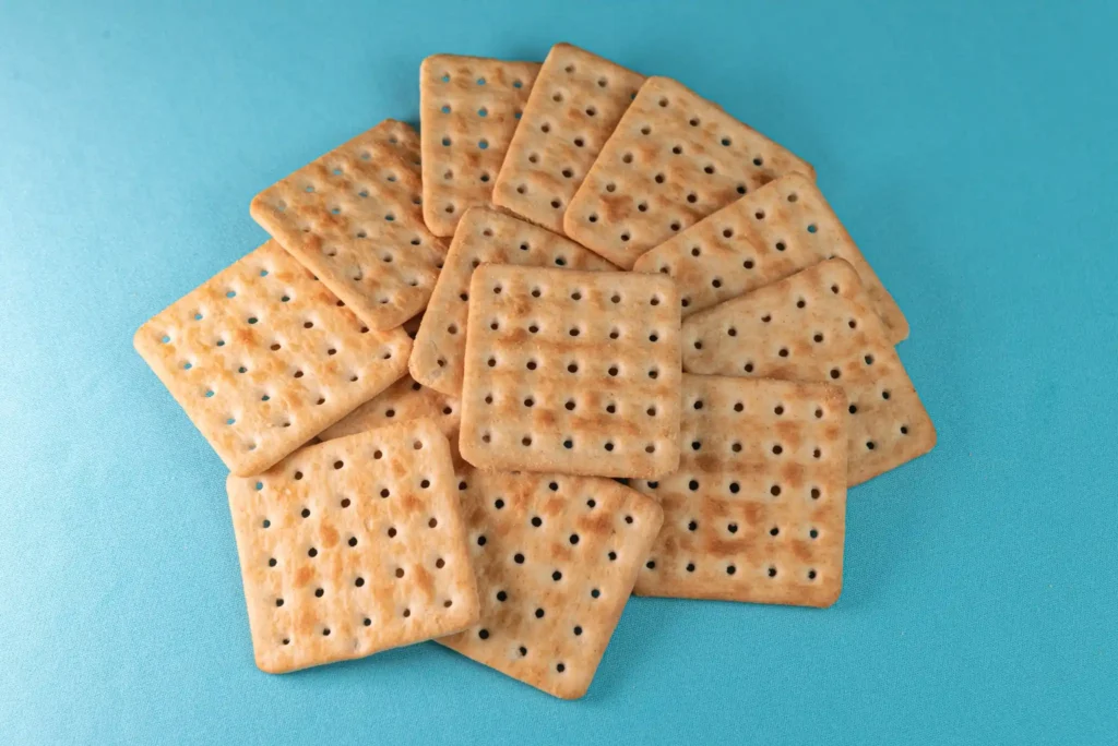 Imagem de biscoitos cream cracker sobre fundo azul, empilhados de forma casual.