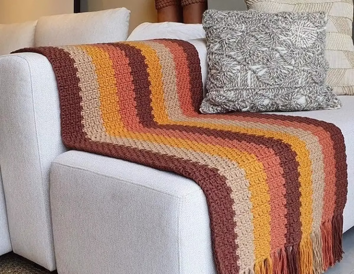 Manta de crochê com listras e franjas decorando sofá branco