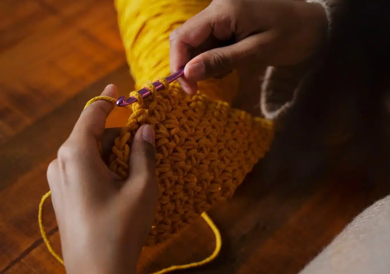 Pessoa tecendo um tapete de crochê com fios amarelos.