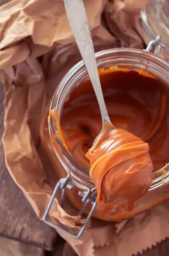 Colher mergulhada em doce de leite caseiro cremoso em pote de vidro