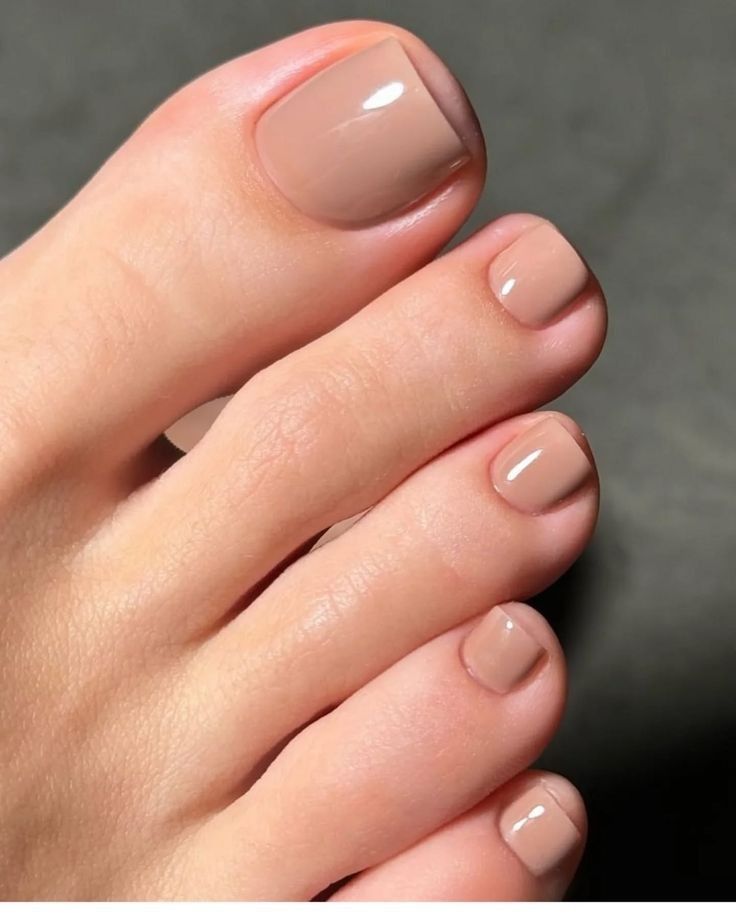 Unhas dos pés pintadas com esmalte nude em acabamento brilhante