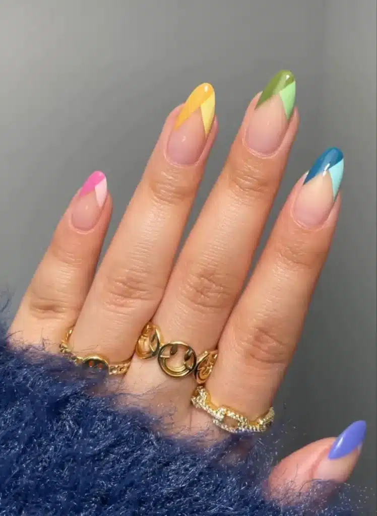 Unhas de francesinha geométrica com pontas triangulares coloridas, em tons de rosa, amarelo, verde e azul.