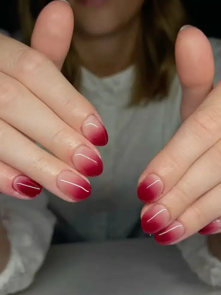 Unhas com efeito francesinha degradê, transição suave de tons vermelhos nas pontas.