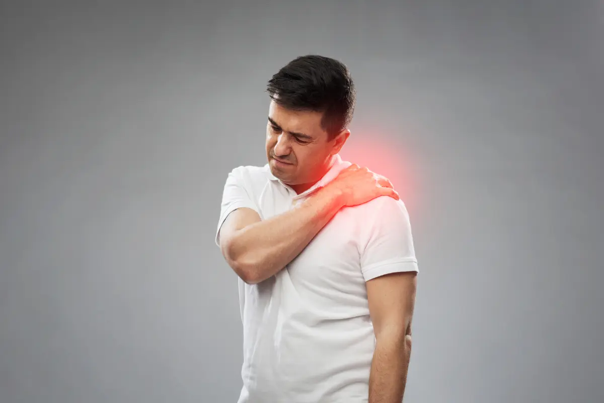 Homem com expressão de dor segurando o ombro.