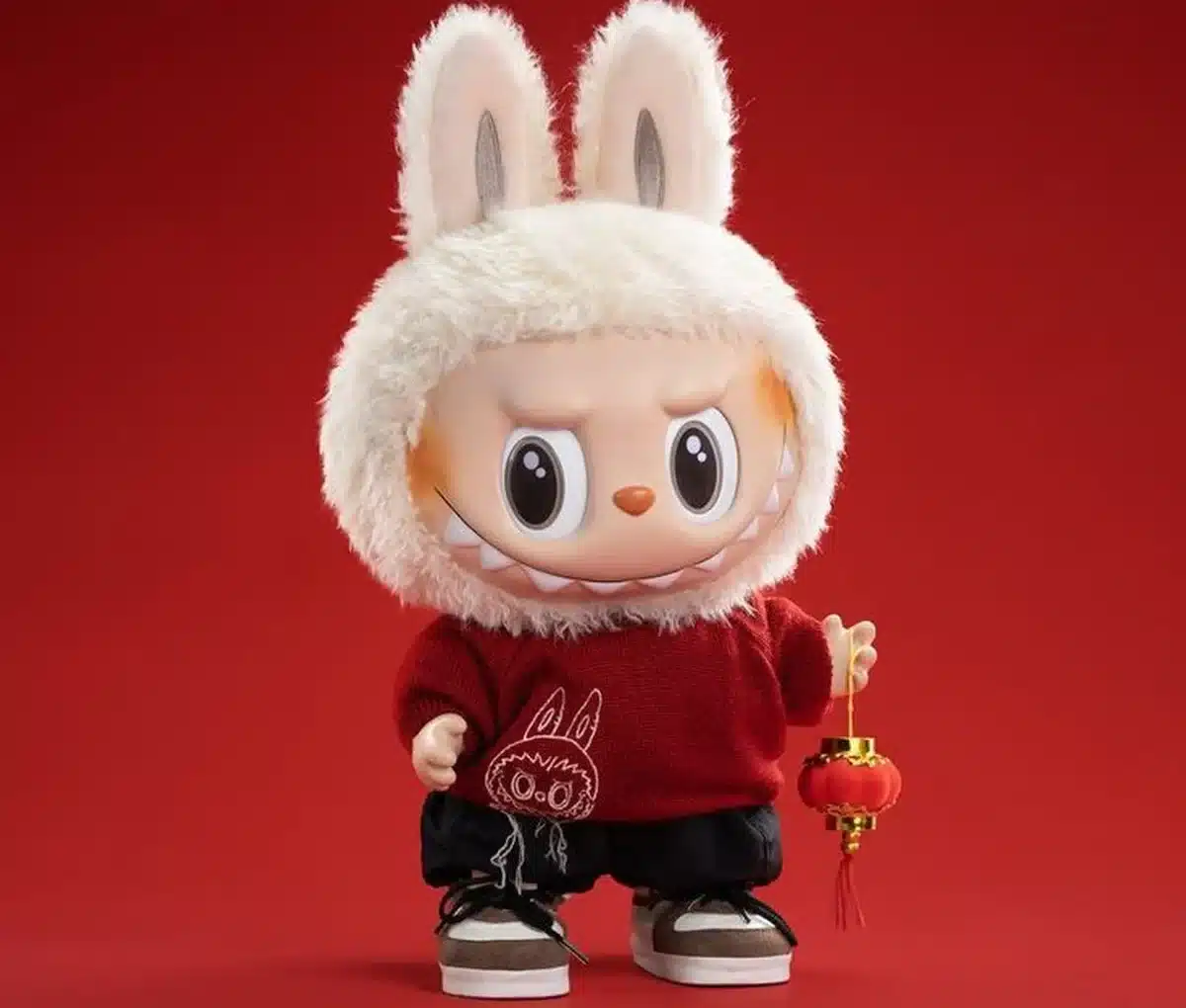 Boneco fofinho com capô de coelho, roupa vermelha e tênis, segurando lanterna de decoração.