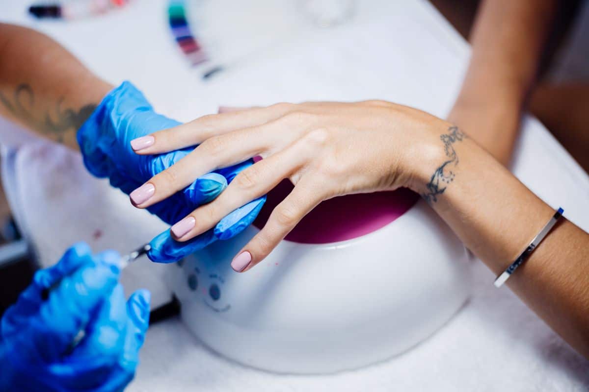 Manicure realizando cuidados em unhas de gel com luvas azuis