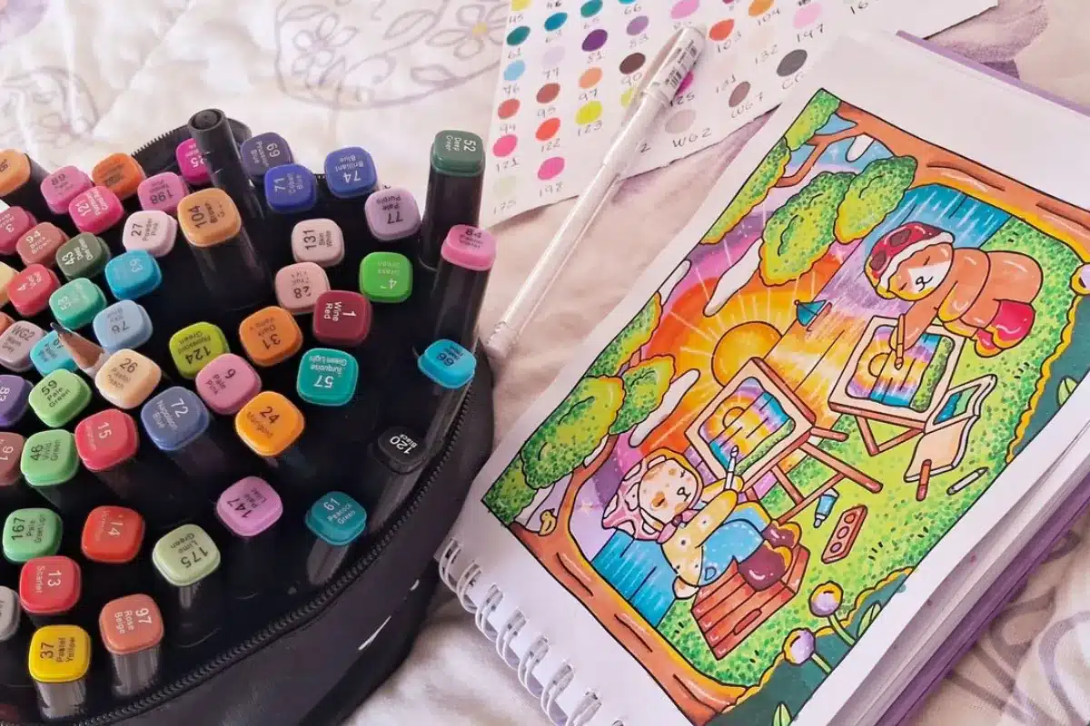 Kit de marcadores coloridos ao lado de um desenho Bobbie Goods colorido com ursinhos pintando ao pôr do sol.