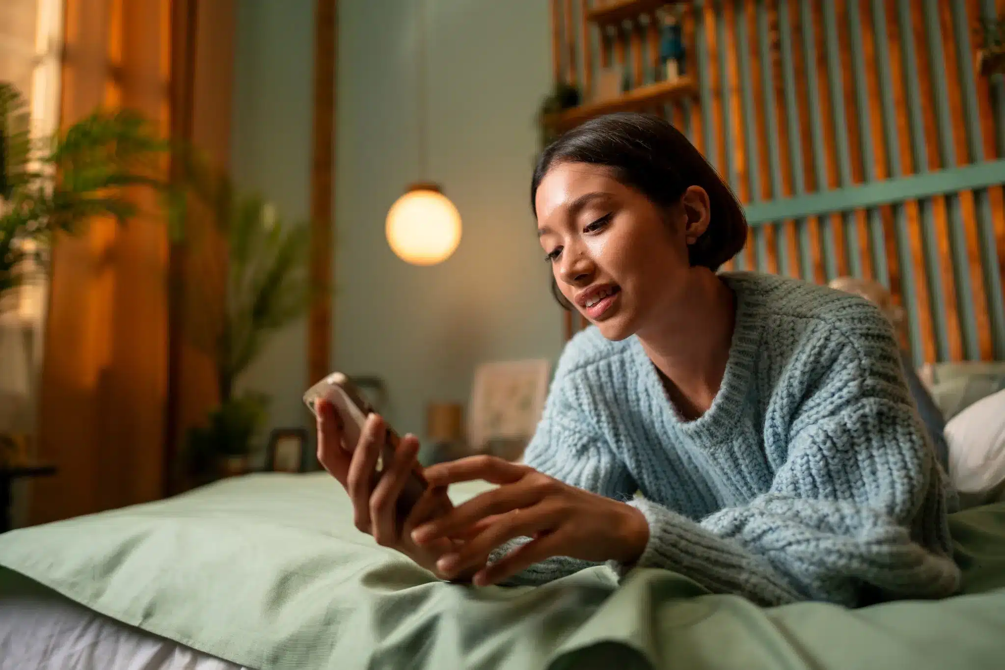 Mulher deitada na cama usando o celular com expressão tranquila