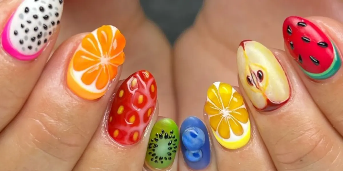 Unhas decoradas com frutas, mostrando nail art criativa com laranja, limão, kiwi, morango, maçã e melancia.