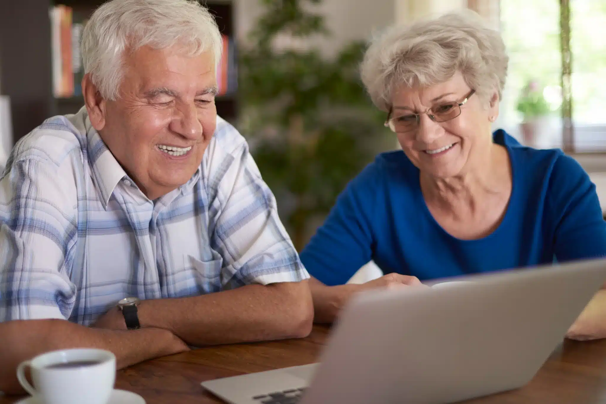 Casal de idosos sorrindo enquanto usam computador, simbolizando o uso de tecnologia e o acesso a benefícios.