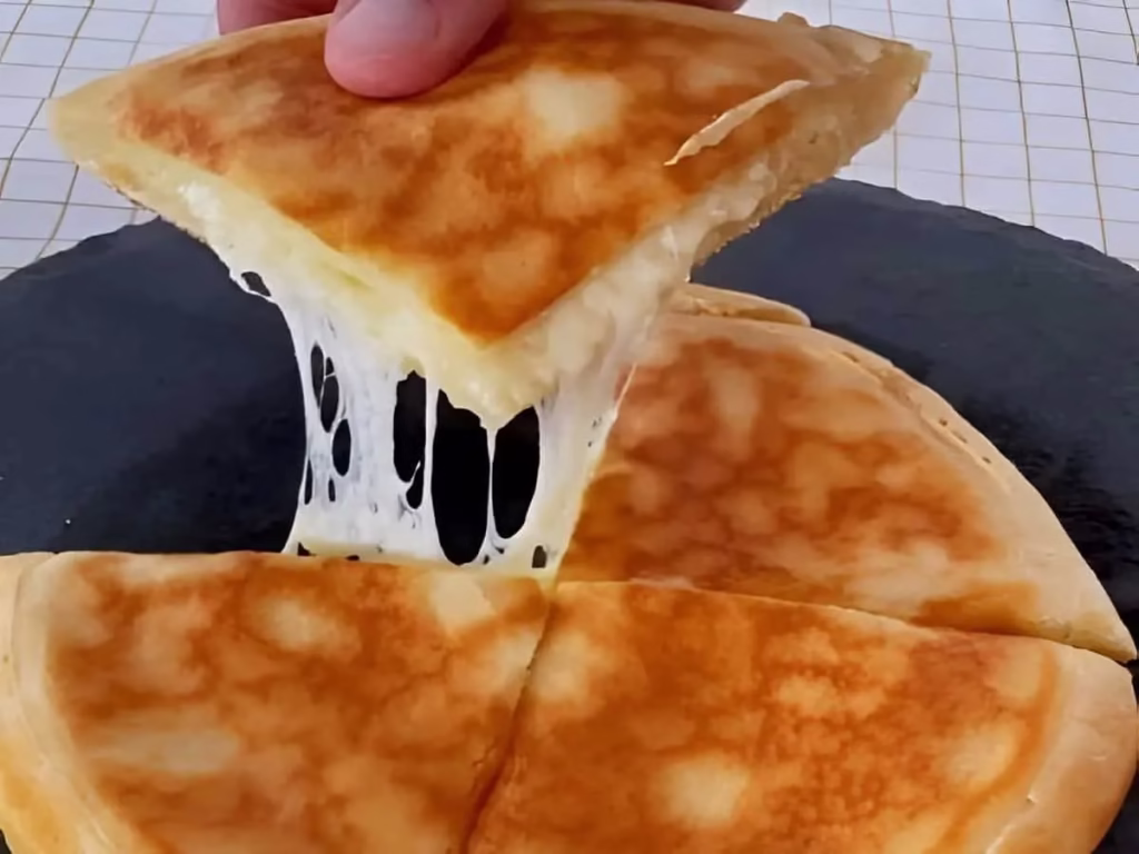 Pão de queijo de frigideira com recheio derretido puxando ao ser cortado