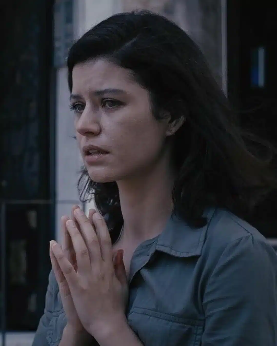 Mulher com expressão de aflição e mãos unidas em gesto de oração.