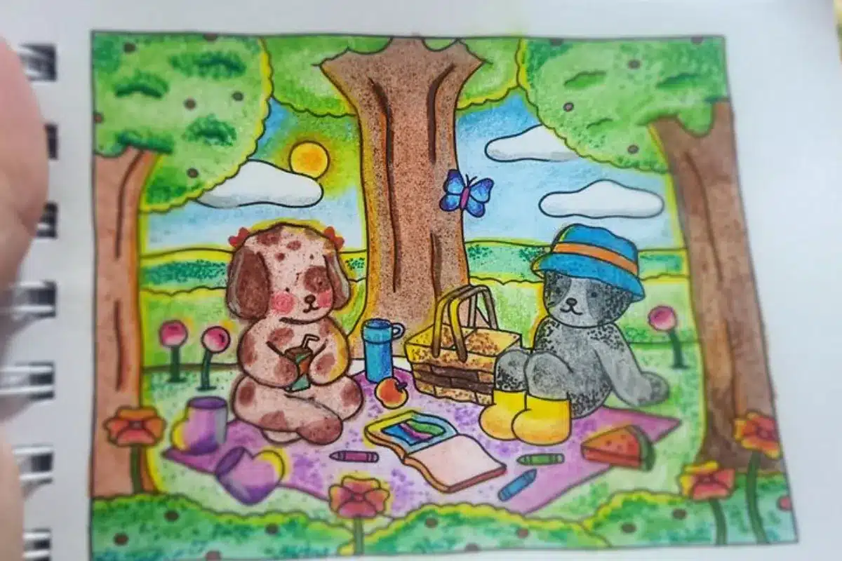 Esta imagem representa dois personagens Bobbie Goods curtindo um piquenique sob o sol em um cenário colorido com árvores, flores, caderno de desenho e lápis espalhados. O céu ao fundo está iluminado e vibrante, transmitindo a sensação de um dia calmo e feliz. Ideal para ilustrar conteúdos sobre pintura emocional com lápis de cor e cenas ao ar livre.