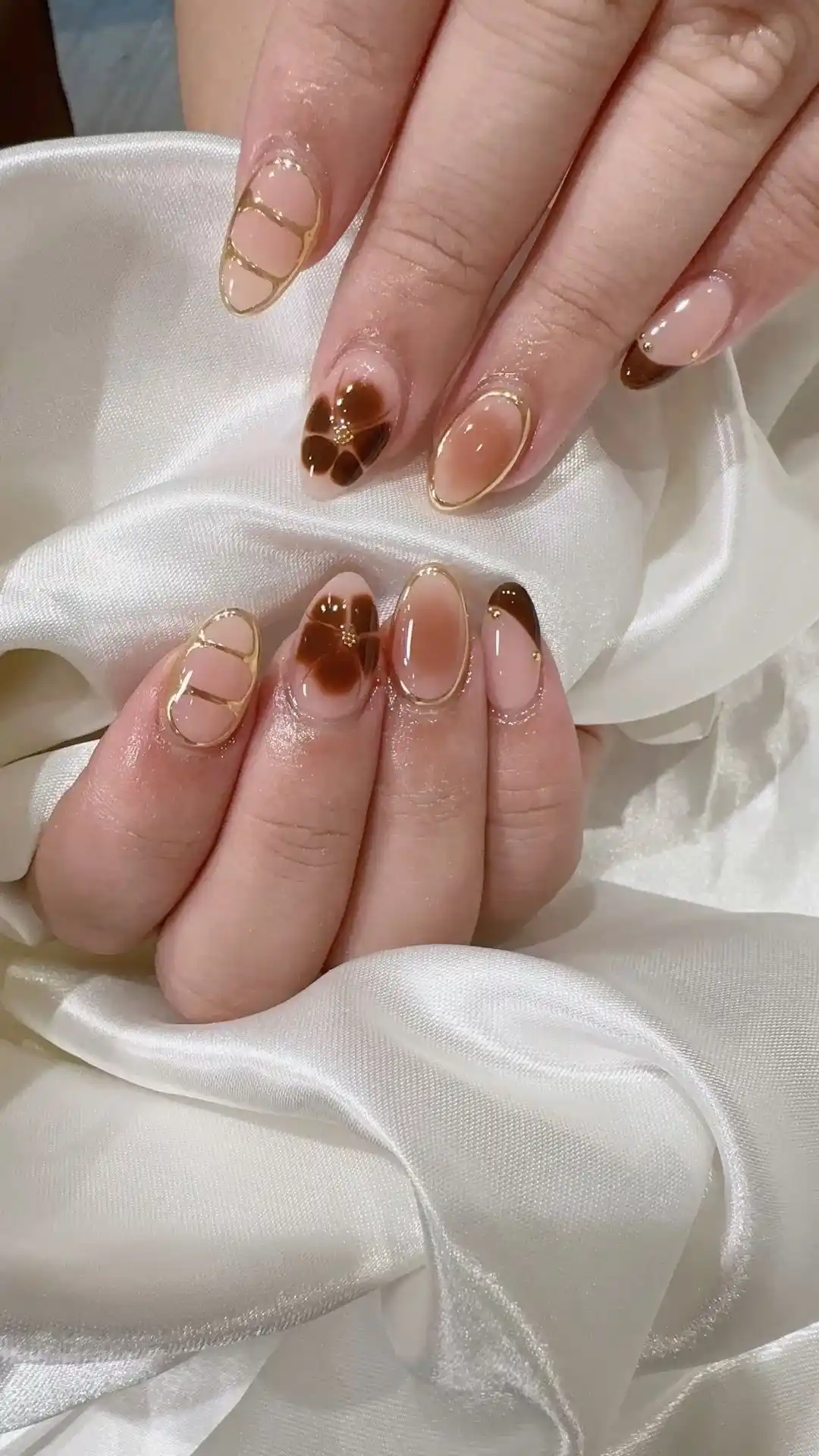 Unhas de porcelana em tons de marrom com detalhes dourados e decoração elegante.