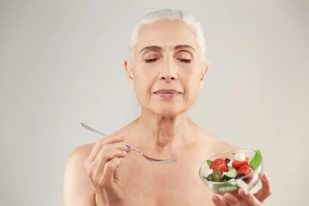 Mulher idosa apreciando uma salada fresca, ilustrando a importância da alimentação para a saúde da pele após os 50 anos.