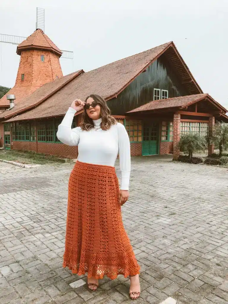 Mulher usando saia de crochê laranja e blusa de manga longa branca, estilo inverno.